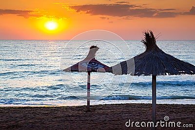 Sunrise on the sea and reed umbrellas on the beach Stock Photo