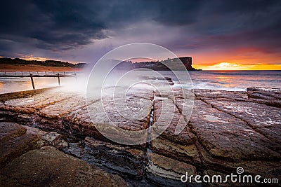 Sunrise sky and waves crash onto rocky beach shore Stock Photo