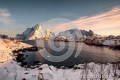 Sunrise on snowy mountain with scandinavian village at coastline in winter Stock Photo