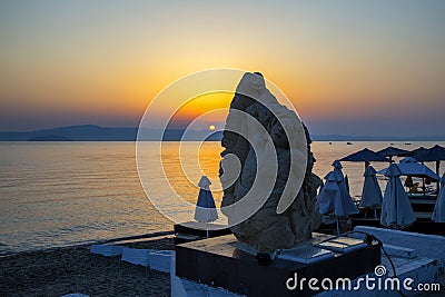 Sunrise and stone carving relief of a human and a snake in Pefkohori Stock Photo