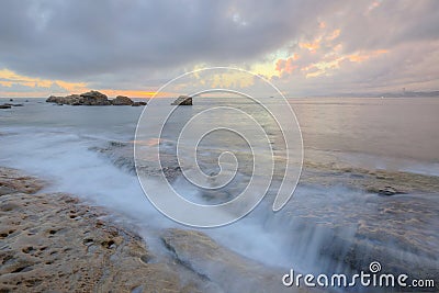 Sunrise under a stormy sky with clouds illuminated by the golden sunlight at the rocky beach Stock Photo