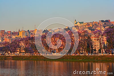 Sunset in Antananarivo city with blossomed jacaranda trees. Houses and historical buildings in back, Anosy lake in front Stock Photo