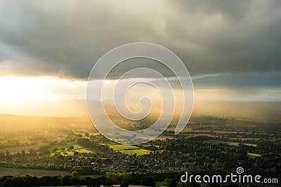 Sunset as sun beams light up the English countryside on a summers evening with dark clouds above. Stock Photo