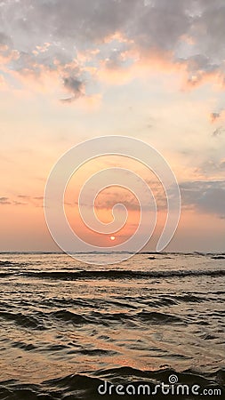 sunset in bali with a calming dark blue ocean and reflected orange skies in between the sand accompinied with her cloud friends Stock Photo