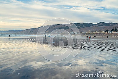 Sunset on the beach. Ocean view, silhouettes of walking people, mountains, and cloudy sky. Pismo Beach, California Editorial Stock Photo
