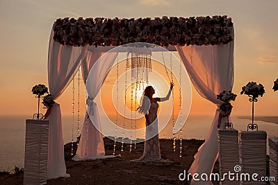 Sunset. bride silhouette. Wedding ceremony arch with flower arrangement with white curtain, outdoor photo. decor. Stock Photo