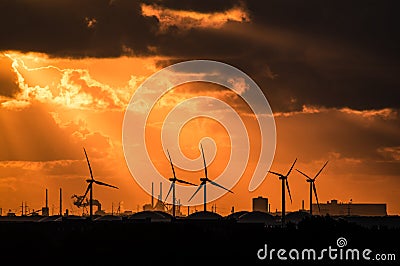 Sunset casting rays through a dramatic orange cloudy sky, onto backlit electric windmills Stock Photo