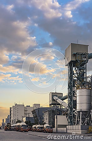 Sunset on concrete mixing transport trucks parked in the Odaiba Bay industrial harbor in front of the Rainbow Bridge of Tokyo Editorial Stock Photo