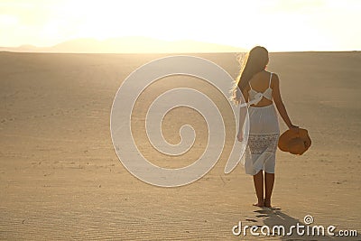 Sunset in the desert. Young woman with white dress walking in the desert dunes with footsteps in the sand during sunset. Girl Stock Photo