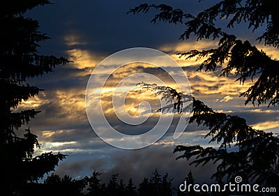 Sunset golden sun rays piercing through dark stormy clouds Stock Photo