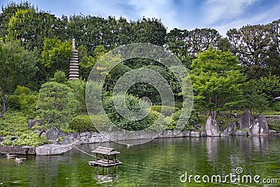 Sunset on hexagonal Gazebo in the central pond of Mejiro Garden where ducks are resting and which is surrounded by rocks and stone Stock Photo