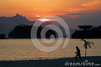 Sunset in Icarai beach with a person walking in the sand, and Ilha da Boa Viagem island in the background Stock Photo