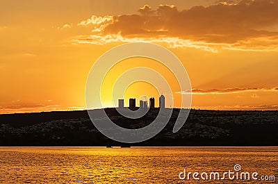 Sunset on a lake with clouds and hill with tall buildings landscape Stock Photo