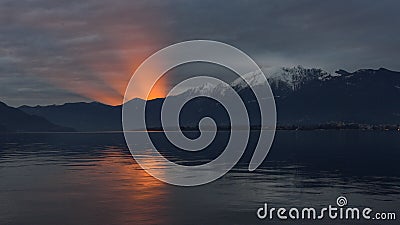 Sunset on the lake with sun setting and creating cone of light emerging from the mountain Stock Photo