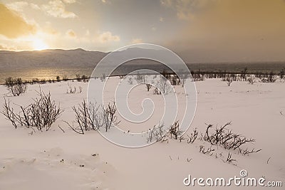 Sunset at the lakeside with rocks of a fjord during low tide in a snowy winter landscape Stock Photo