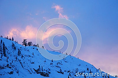 The sunset light hits a wispy cloud over a snowy mountain Stock Photo
