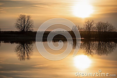 Sunset in the meadow. The sun, sky and trees are reflected in the river. Spring flood Stock Photo