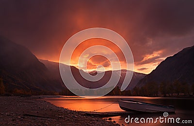 Sunset In The Mountains. Enchanting Autumn Mountain Landscape In Red Tones With Sunset Sky, River with Reflection And Lonely Boat. Stock Photo