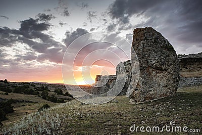 Sunset on the night of the summer solstice with a megalithic menhir in the foreground and a rocky mountain formation in the Stock Photo