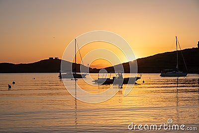 Sunset orange color over sea water. Boats anchored at Vourkari port, Kea island, Greece Stock Photo