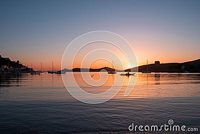 Sunset orange color over sea water. Boats anchored at Vourkari port, Kea island, Greece Stock Photo