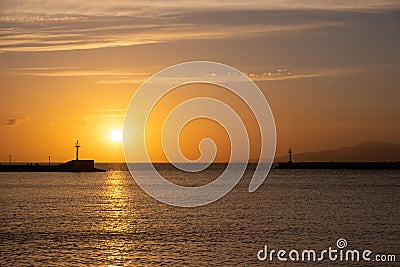 Sunset over Mykonos island, Cyclades, Greece. Lighthouse, orange yellow sky sparkle sea. Vertical Stock Photo