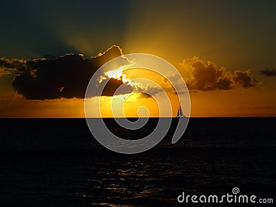 Sunset over the Ocean with Beams of Light and Silhouette of Sail Stock Photo