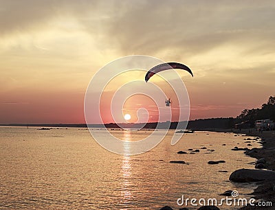 Sunset over the sea. Reflection of the sun in water. Silhouette of paraglider flying in the sky. Sunset beach in a summer evening Stock Photo