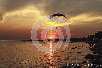 Sunset over the sea. Reflection of the sun in water. Silhouette of paraglider flying in the sky. Sunset beach in a summer evening Stock Photo