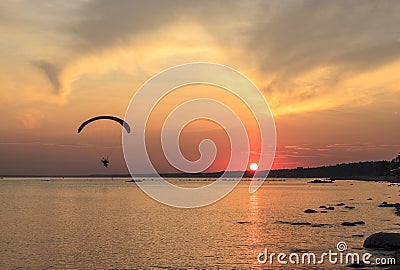 Sunset over the sea. Reflection of the sun in water. Silhouette of paraglider flying in the sky. Sunset beach in a summer evening Stock Photo