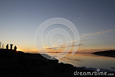 Sunset over water with three people in the shadow with whisp of clouds Stock Photo