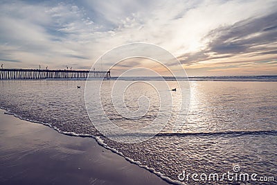 Sunset in pink color. Pacific ocean, wooden pier, and sun setting down the horizon with beautiful sun reflections on water. Stock Photo