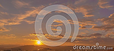 Sunset scene with sun fall behind the clouds and mountains in background, warm colorful sky with soft clouds Stock Photo