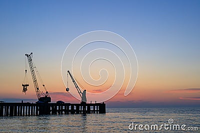 Sunset at sea, evening at sea. against the background of a beautiful sky, a silhouette of a pier with lifting mechanisms Stock Photo