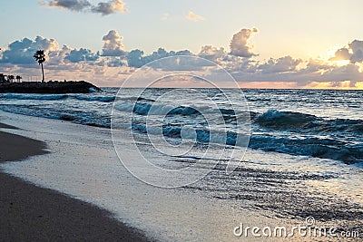 Sunset at the sea. Turquoise water in the ocean in the evening. Yellow sky with small clouds and blue waves at sandy beach at the Stock Photo