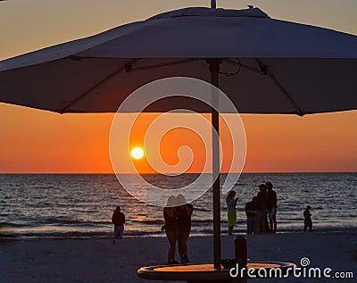 The sunset with the silhouette of an umbrella and people on the beach. This is at Indian Rocks Beach, Gulf of Mexico, Florida. Editorial Stock Photo
