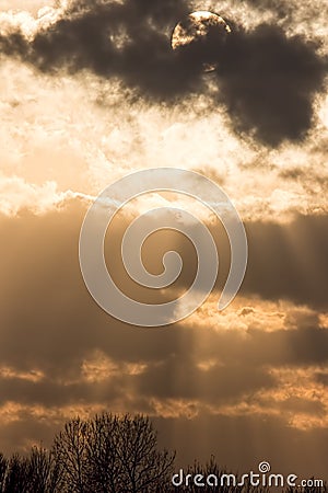 Sunset sky background, Sun behind dark cloud with crepuscular ra Stock Photo