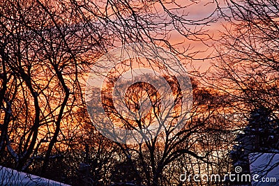 Sunset after a snowstorm glows red and orange over snow-covered trees and roofs. Stock Photo