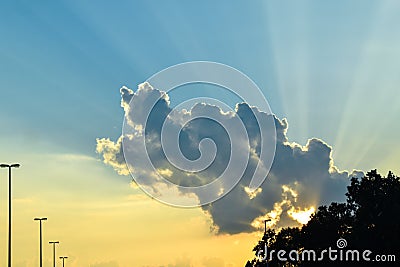 Sunset with sun behind cloud. Yellow sun rays with blue sky Stock Photo