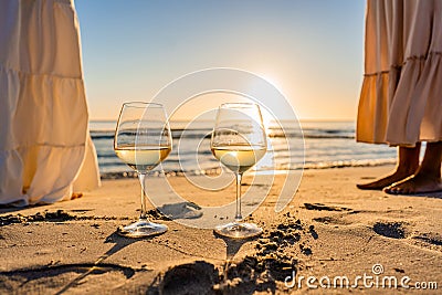 Sunset or sunrise beach party scene with two unrecognizable multiracial boho girls wearing long white dress barefoot on the ocean Stock Photo