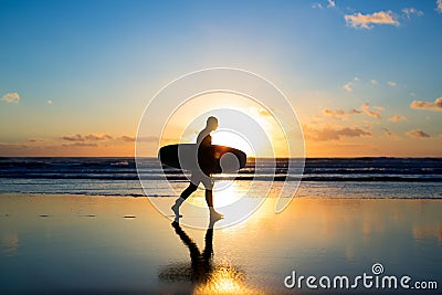 Sunset surfing. Silhouette of man surfer walking with a surf board in his hands across the ocean shore. Stock Photo