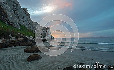 Sunset twilight colors and sand swirls at Morro Rock on the central coast of California at Morro Bay California USA Stock Photo