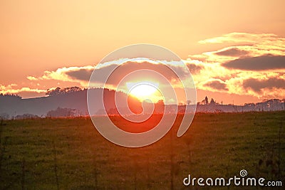 Sunset view over the field red sun setting behind clouds making sky golden Stock Photo
