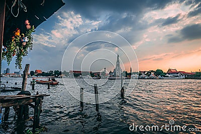 Sunset at Wat Arun. Chao Phraya with Longboat at Sunset. View from a Restaurant with some tourists inside. Editorial Stock Photo