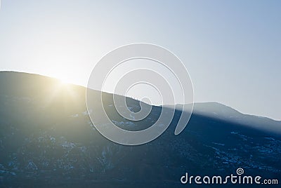 A sunset at the winter mountains, last yellow evening sun light rays over the mountain landscape and long shadows Stock Photo