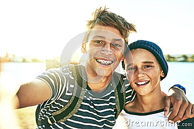 Sunshine always makes for a good selfie. Cropped portrait of two young brothers taking selfies outside with a lagoon in Stock Photo