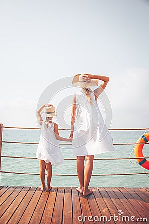 Suntanned woman and girl in white dresses enjoy sea view at the wooden pier Stock Photo