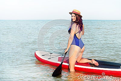 Sup boarding. A woman in a hat and blue swinsuit poses standing with a sup board. Stock Photo