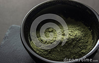 Super food or marijuana kief concept.Green powder in a small ceramic bowl, on a stone stand, on a black background. Stock Photo