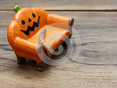 Super or giant worm crawling on orange miniature ceramic pumpkin couch or sofa over dark wooden surface Stock Photo